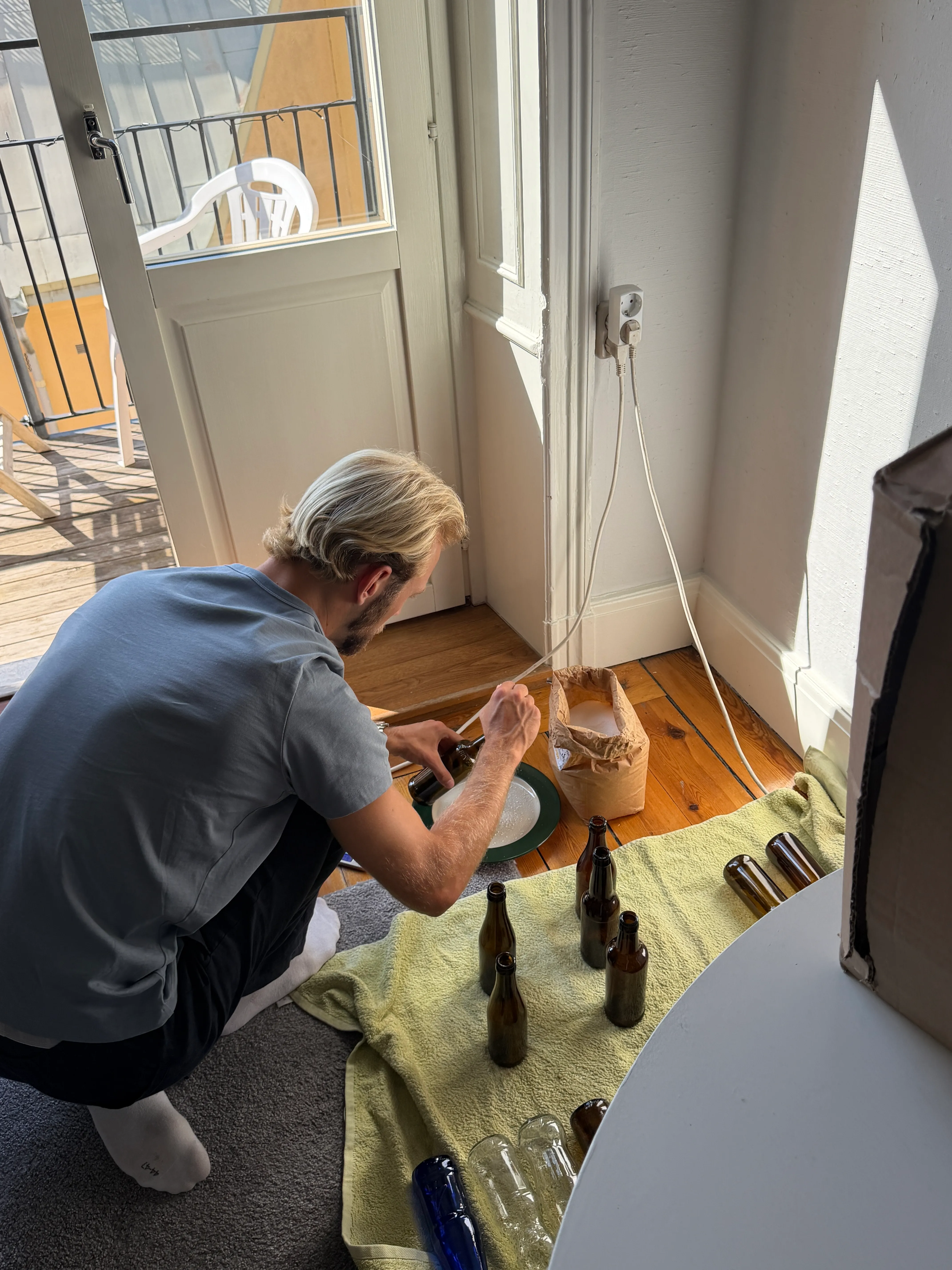 Marcus filling brown beer bottles beside the balcony door.