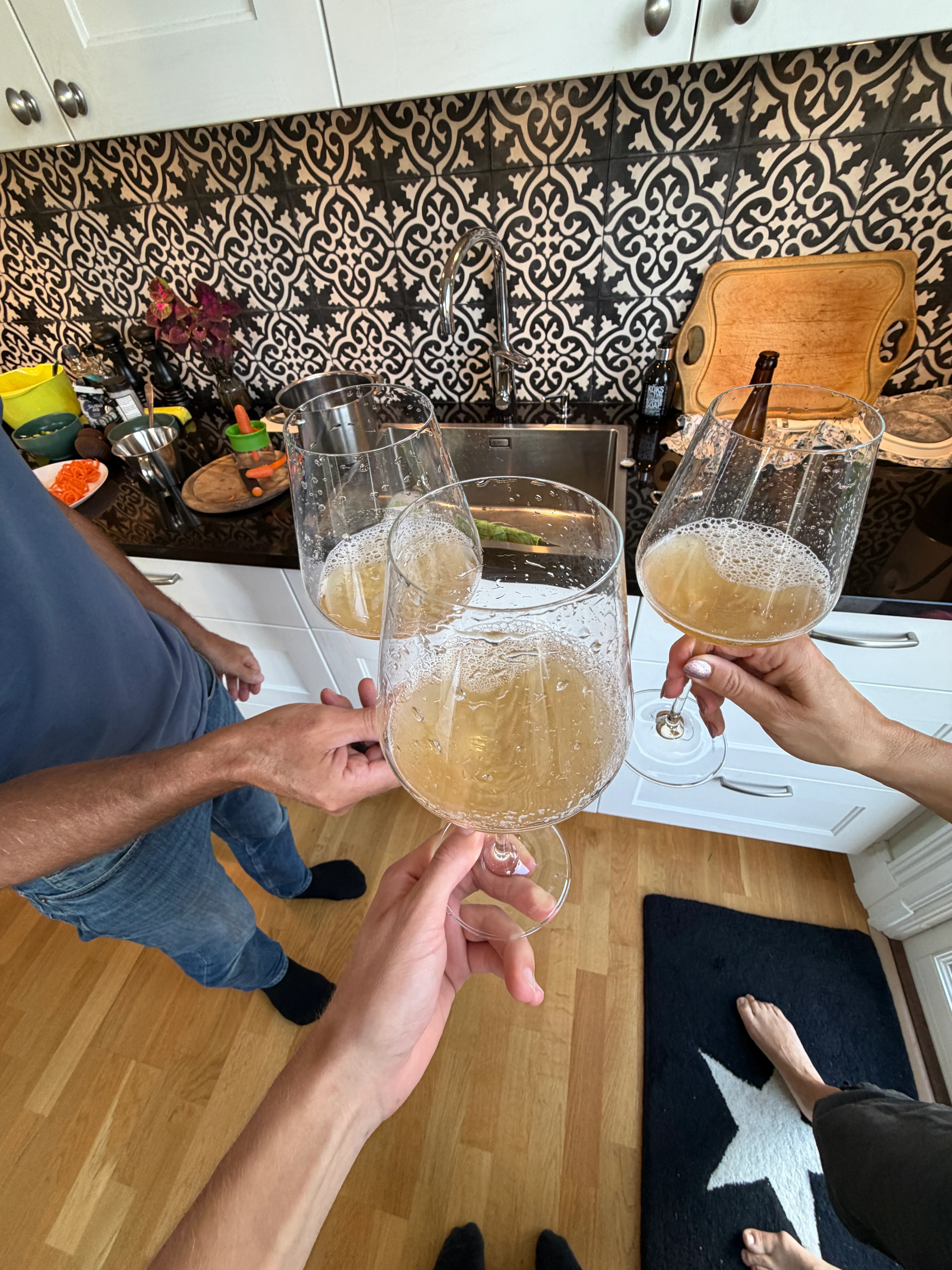 Three glasses of pale golden beer raised together in the kitchen.